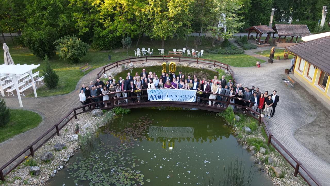Alumni posing on a garden footbridge with gold number ten balloons and an AIESEC Alumni Europe banner