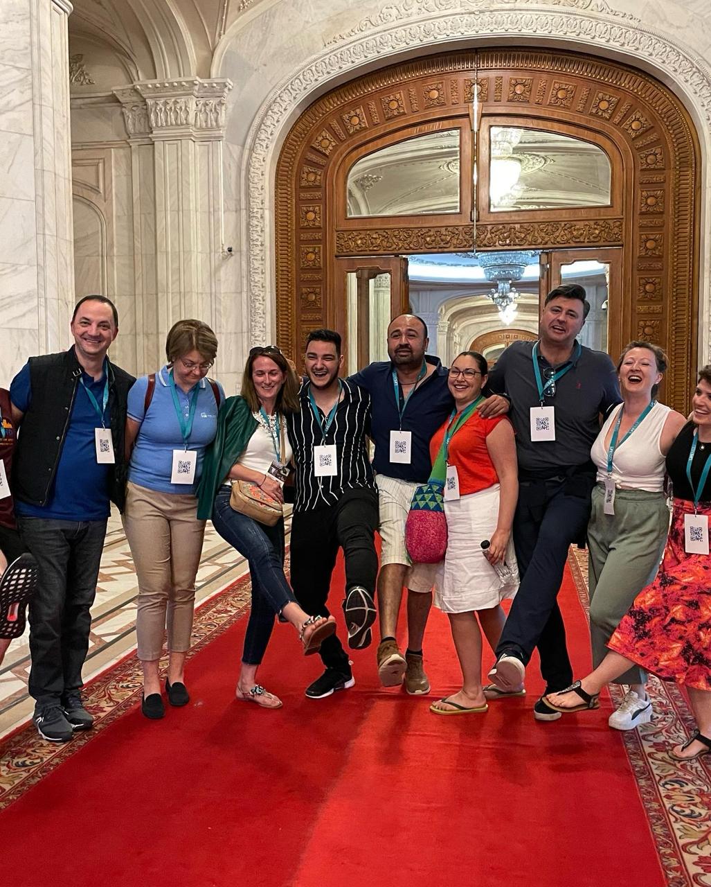 Alumni posing playfully on a red carpet in an ornate palace hall